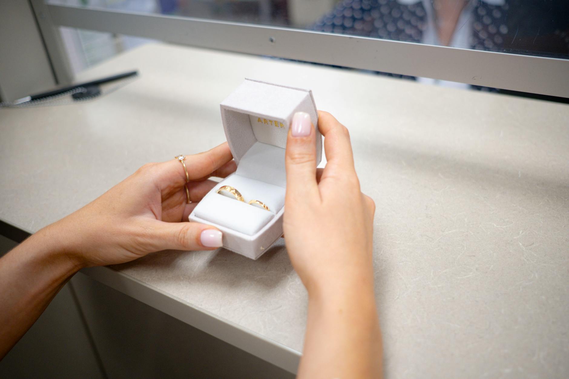 Dłonie otwierają pudełko z obrączkami przy ladzie sklepowej