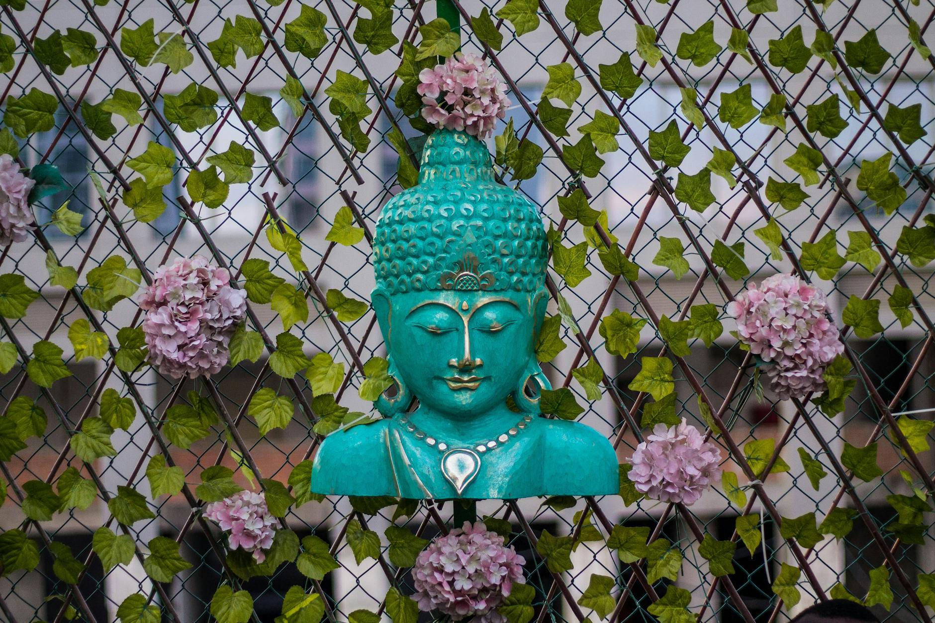 Turkusowa figura Buddy na tle kwiatowych pnączy