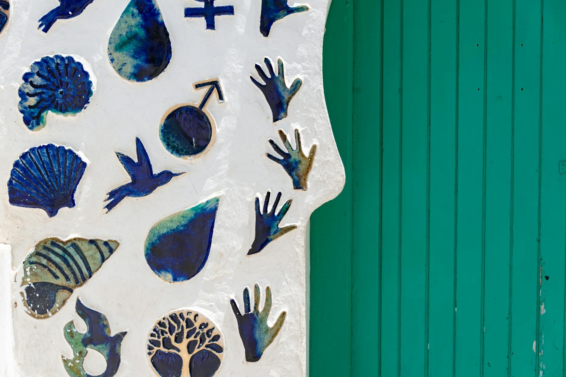 Turkusowe drzwi wśród niebieskich ceramicznych symboli na ścianie