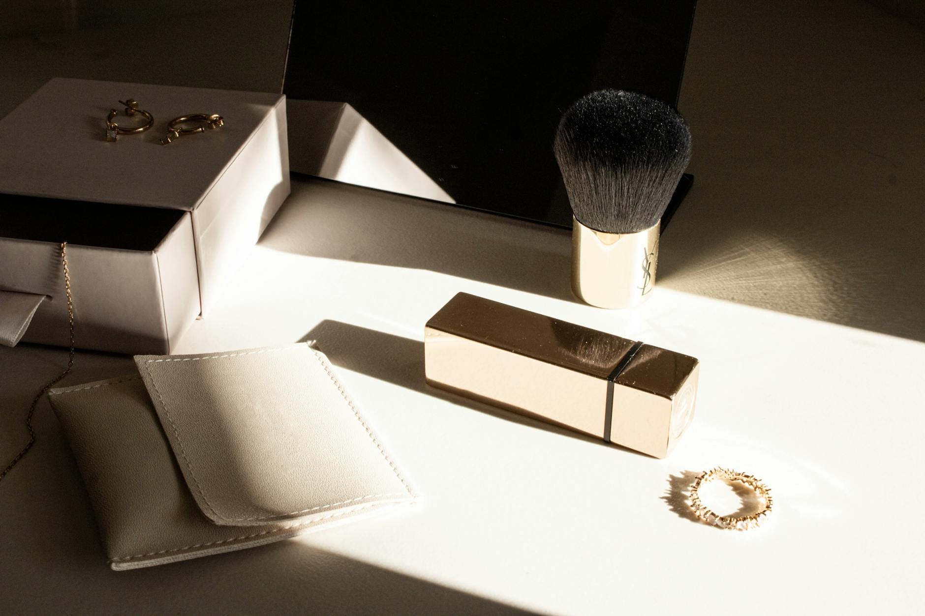 Złote dodatki i kosmetyki ułożone w słońcu na jasnym blacie