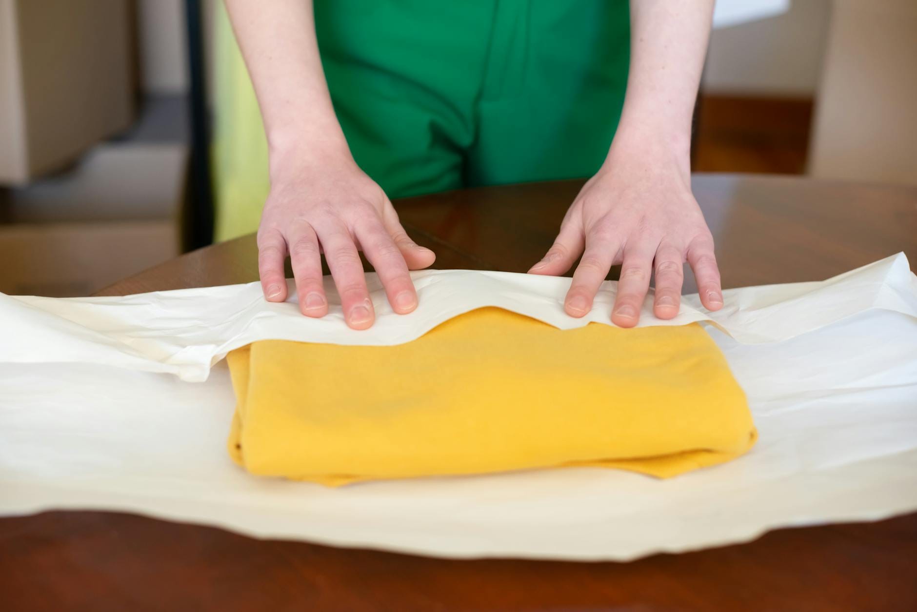 Dłonie ostrożnie zawijające żółtą tkaninę w papier podczas pakowania