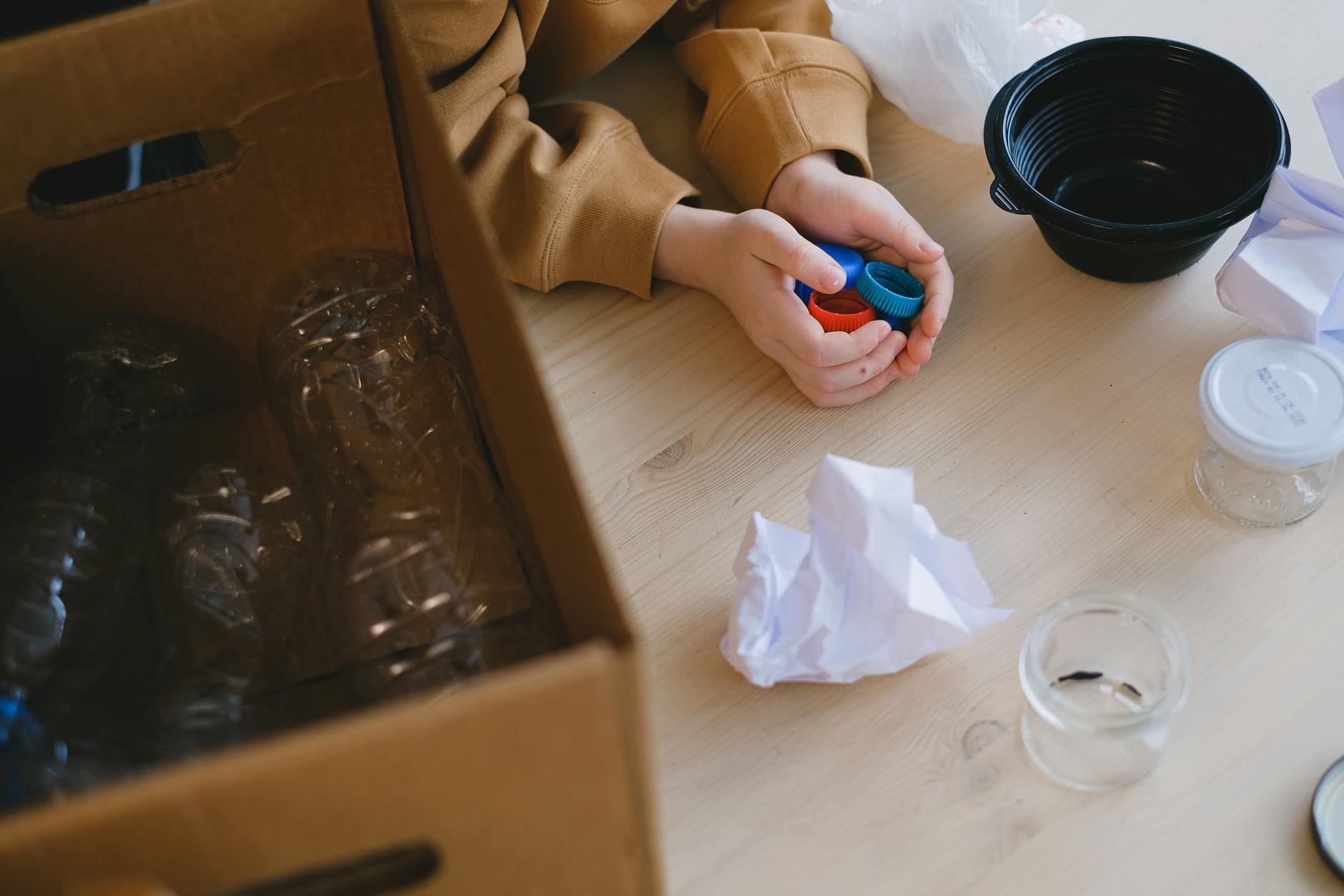 Osoba segreguje plastikowe nakrętki i papier na stole