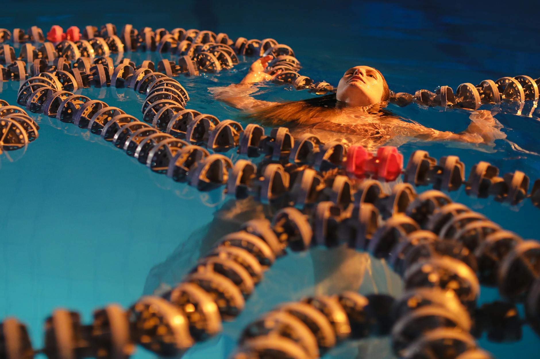 Kobieta unosząca się w nocnym krytym basenie z chlorowaną wodą